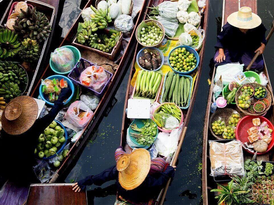 Floating-market vendors in conical hats with boats full of fresh produce — bananas, limes, herbs.